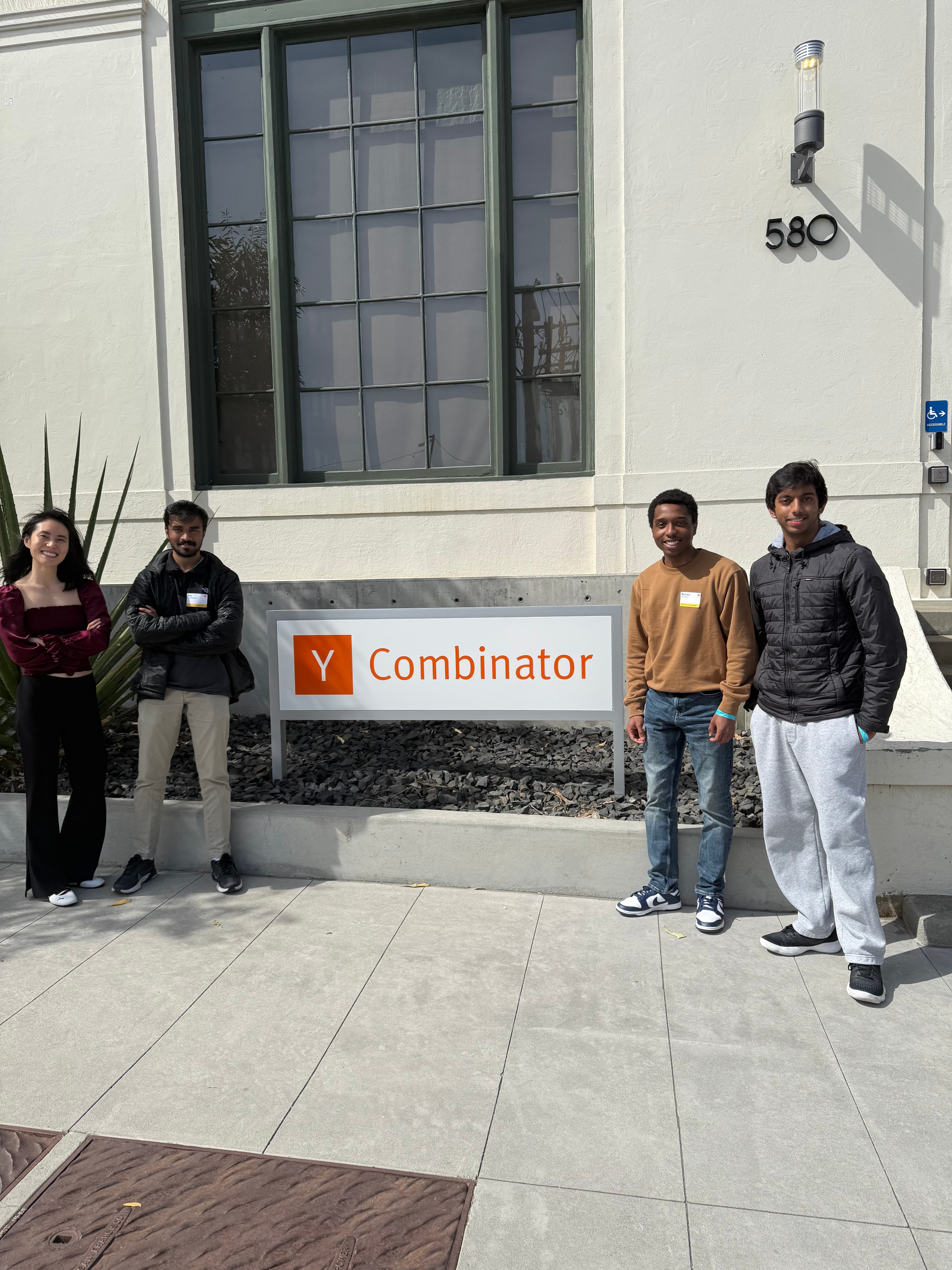 Four people standing beside a Y Combinator sign outside a building